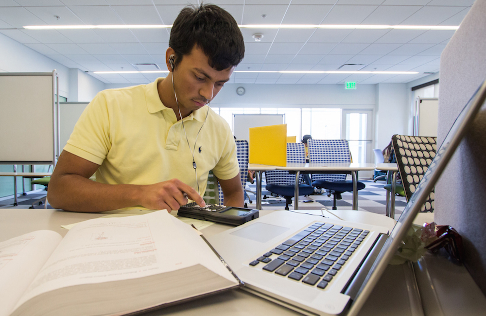 Student with a book, computer, and calculator at the CULC.