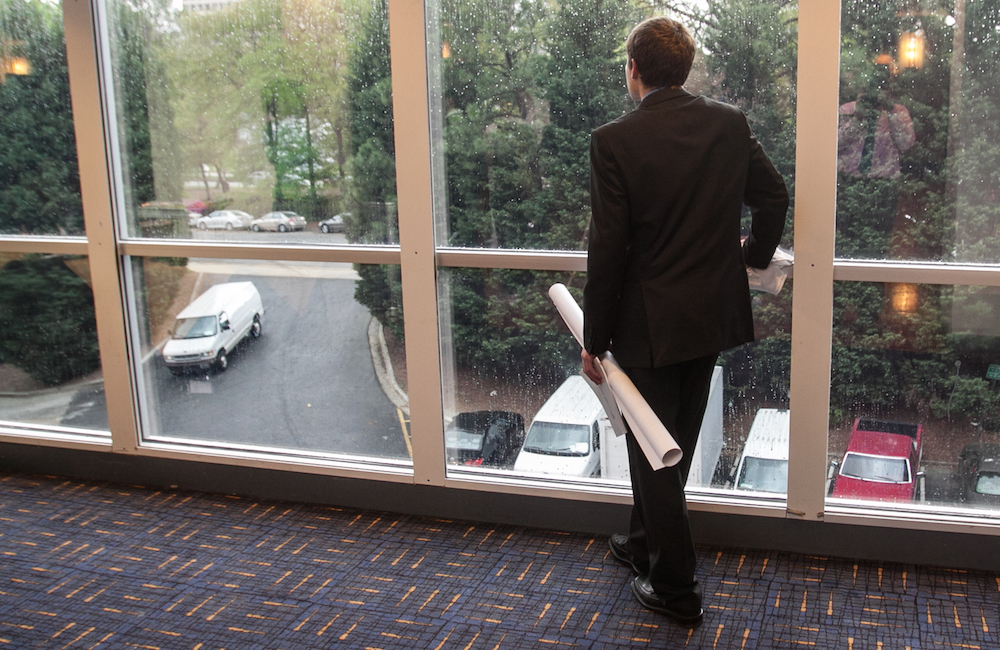 Student holding his research poster at the symposium, looking out a window.